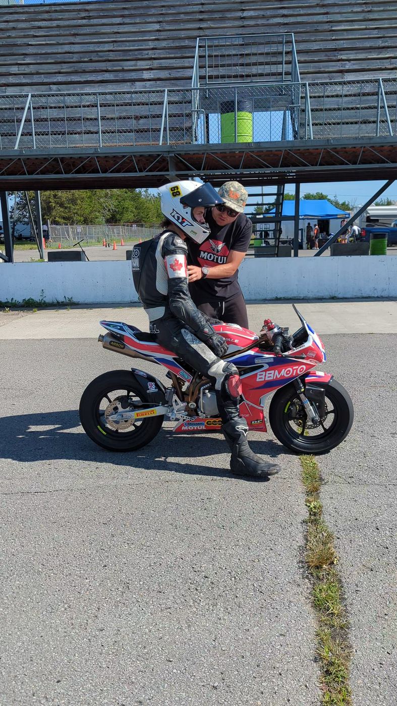 A young racer in full leathers being helped on an Ohvale in the paddock