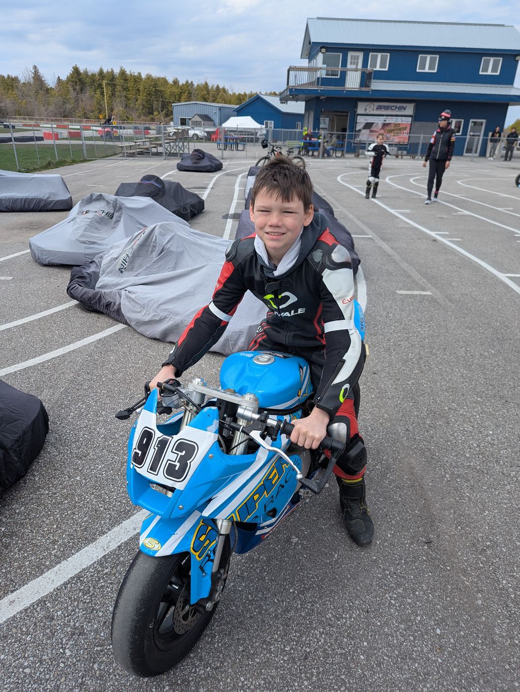 A grinning young rider in full leathers sitting on his blue 913 Ohvale in the Brechin paddock