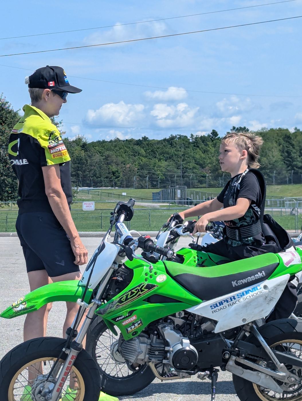 Toni Sharpless coaching a young rider beside a Super Sonic Road Race School bike